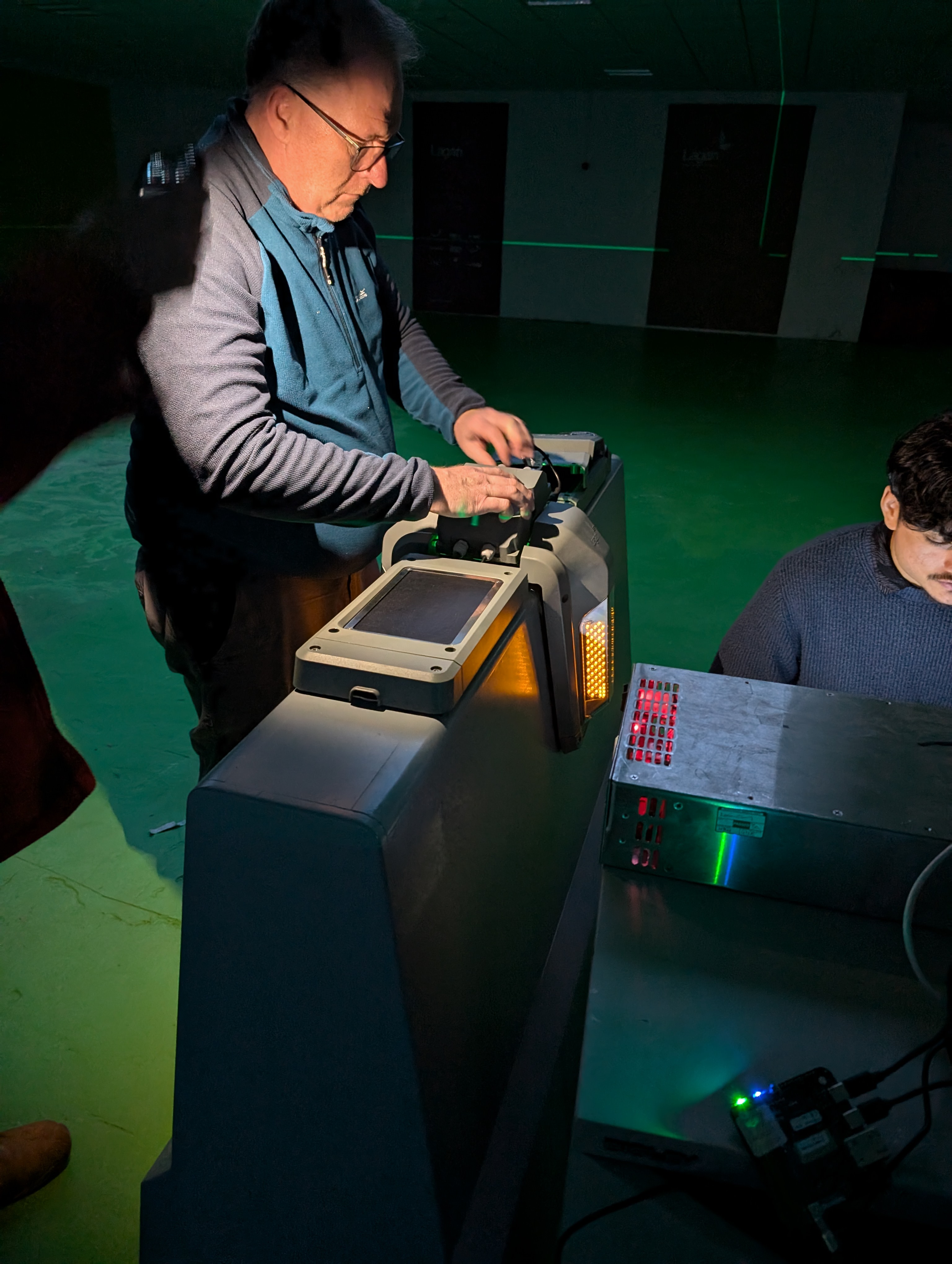 An engineer calibrating a roadside warning unit indoors, its amber and red LED array lit, alongside a rack-mounted control unit.