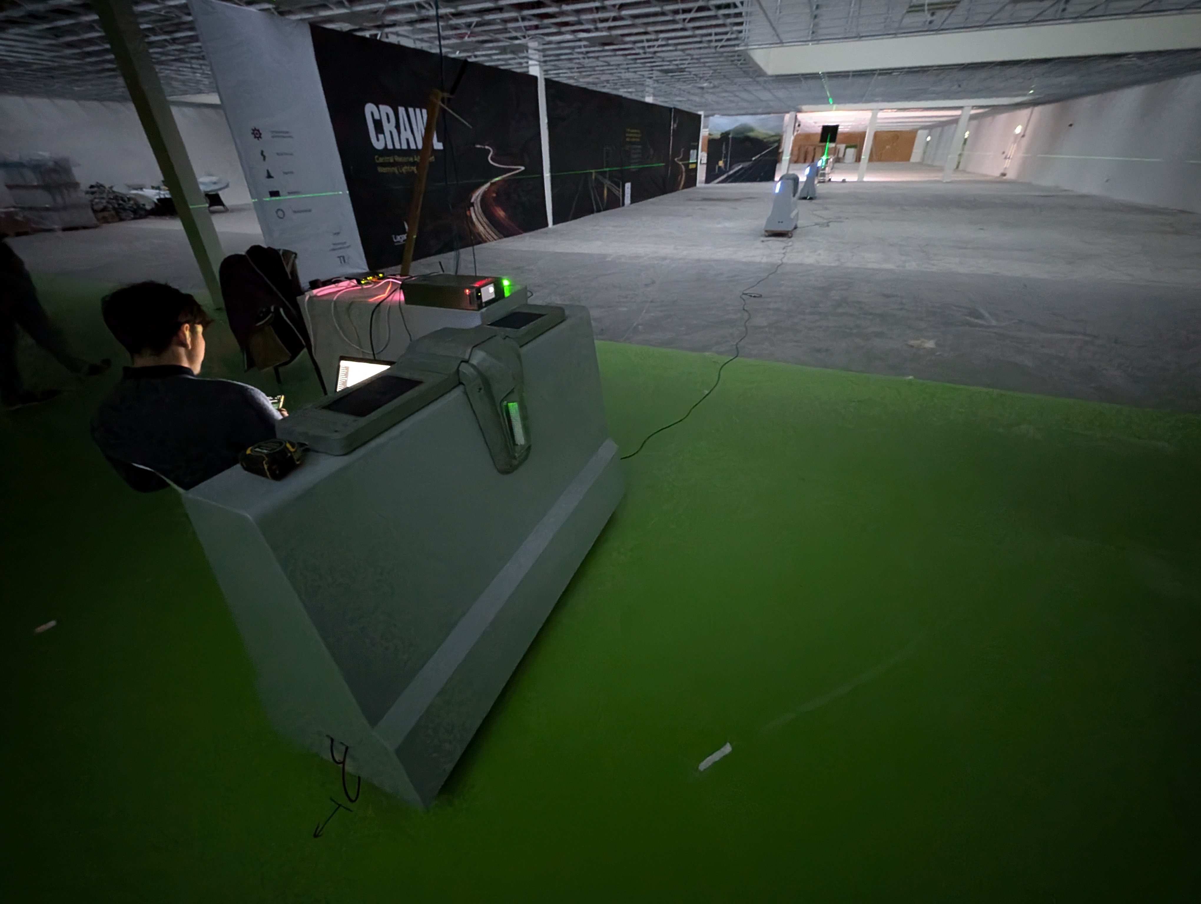 Two roadside warning units being tested indoors on a lab floor marked out with laser reference lines, in front of a banner reading CRAWL — Central Reserve Active Warning Lighting.